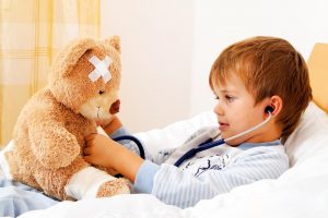 Little boy in bed checking his teddy bear's heartbeat with a stethoscope