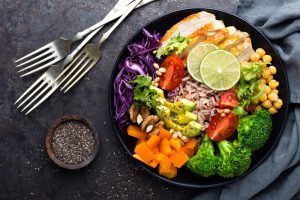 Colorful plate of healthy foods like broccoli, carrots, chicken, tomatoes, brown rice