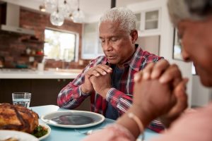 Older man and wife sitting at table praying over meal