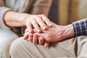 Focus on hands, younger person holding older person's hand in a comforting way