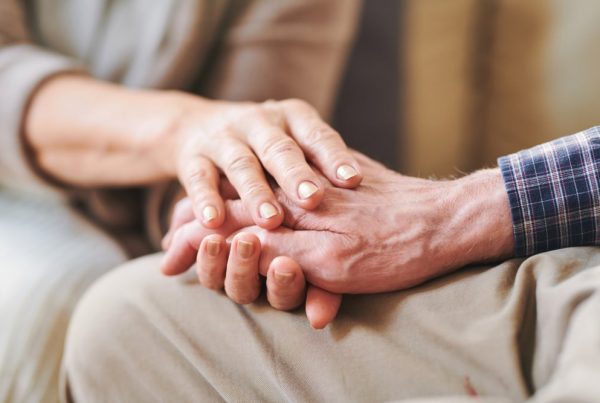 Focus on hands, younger person holding older person's hand in a comforting way