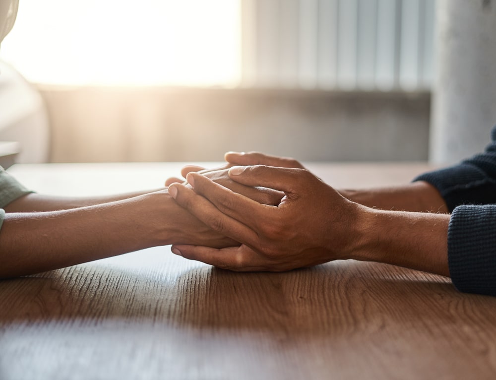 Two people holding hands across table, no faces