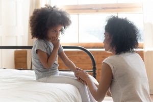 Child sitting on bed with mother kneeling and talking in a loving way