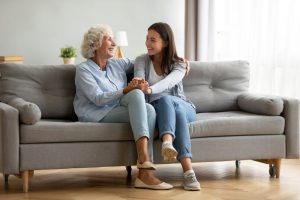 Mother and adult daughter sitting on couch together, talking and lighthearted