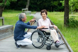 Man crouched beside wheelchair-bound wife, talking and laughing