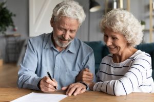 Mature man and wife sitting at table signing documents