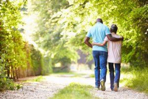 Man and woman walking on a green path outside, arms around each other's waist