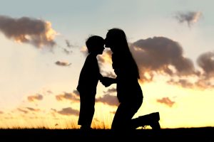 Mother kissing son's forehead at sunset