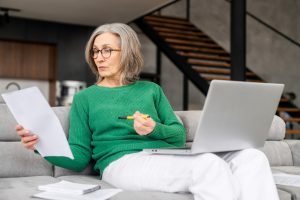 Older woman wearing green sweater sitting on couch doing research