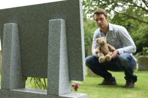 Man laying teddy bear at grave