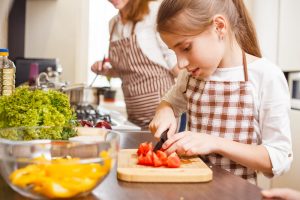 Little girl cutting vegetables in the kitchen with mother