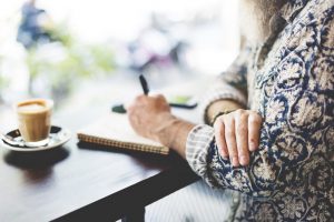 Woman sitting at table, writing on notepad