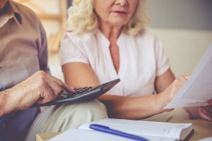 Older man and woman using calculator to add up costs