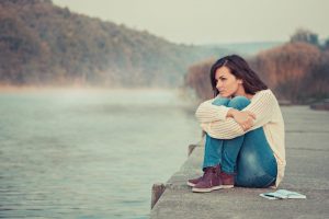 Young woman thinking as she sits beside lake