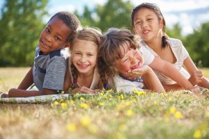 Four children of different ethnic backgrounds smiling while playing outside