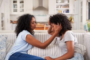 Mother comforting daughter, sitting on couch