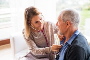 Home health nurse checking older man's heartbeat with stethoscope