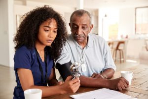 At home nurse taking older man's blood pressure