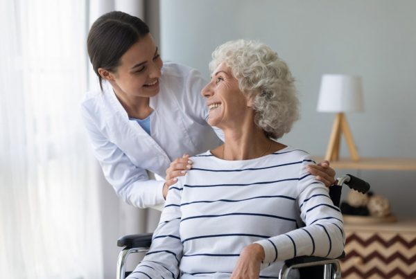 At home aide smiling at and helping elderly female patient
