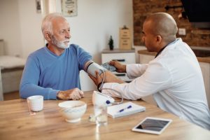 Older man sitting with doctor, getting his blood pressure taken