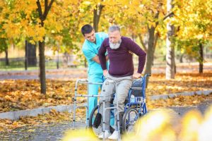 Male at-home nurse helping older man stand up from wheelchair