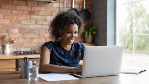 Young woman smiling at laptop camera and writing a comment