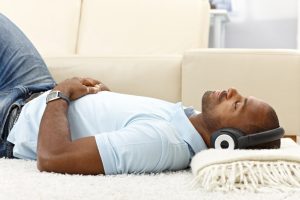 Man in light blue shirt relaxing on the floor and listening to music with headphones