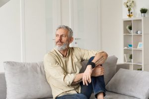 Mature man sitting on couch at home as he thinks