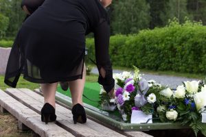 Shows a woman placing flowers on a grave as a remembrance