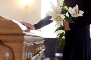 Shows a young woman standing next to a casket with white lilies