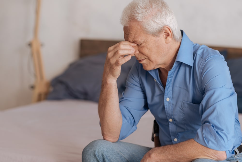 Shows grieving man sitting on bed as he pinches his brow