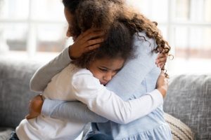 Mother holding school-age daughter close in a comforting way