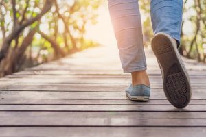 Person walking on a wooden walkway in a park, focused on the person's calves and shoes