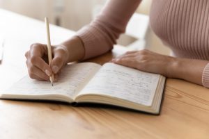 Woman sitting at table and writing letter to lost loved one