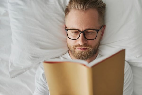 Man with beard lying in bed reading a book