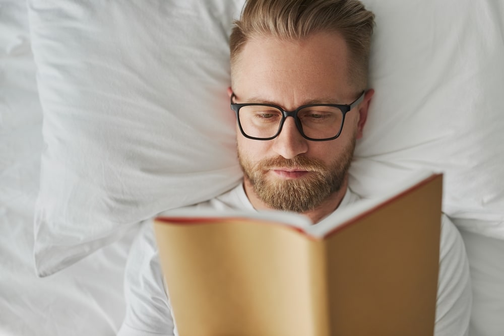 Man with beard lying in bed reading a book