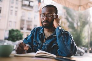 Man quietly sitting at an outdoor cafe while writing in a journal