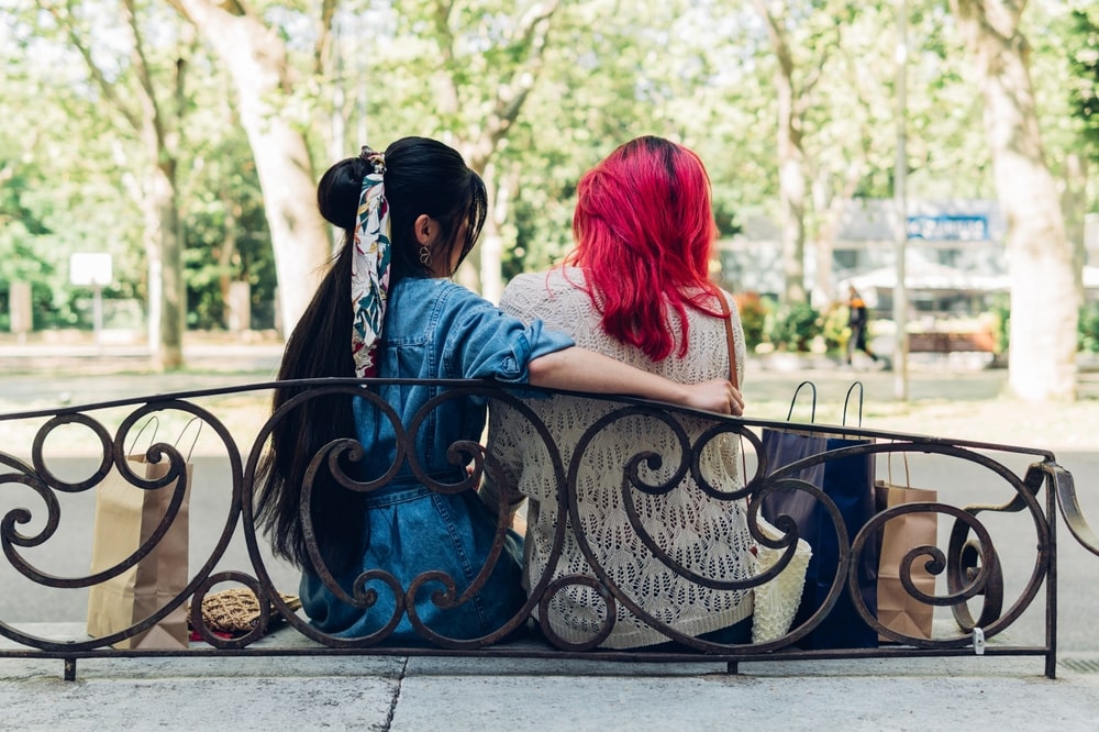 Two female siblings sitting on a bench outdoors spending time together