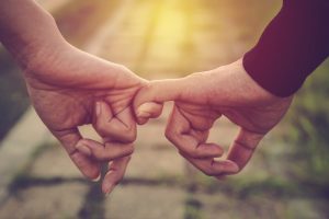 Two people holding hands by hooking pinkies together