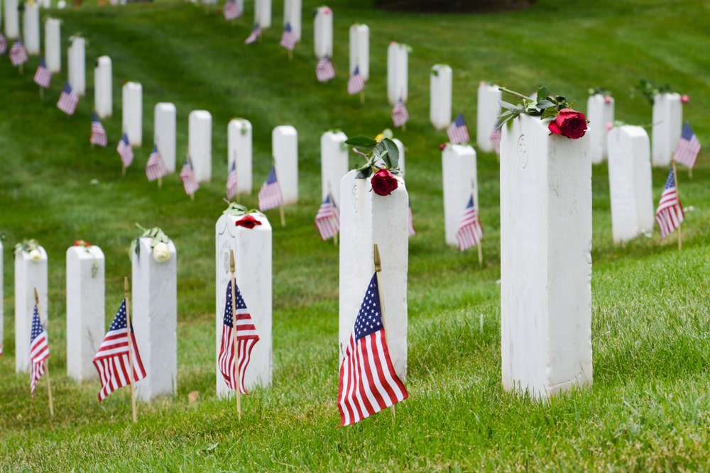 Well-kept headstones with flags and roses in a green national veteran cemetery