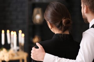 man and woman at funeral, his arm around her shoulder in a comforting way