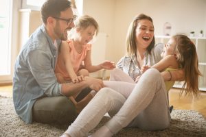 Happy family with two daughters playing at home. Family sitting on floor and playing together.