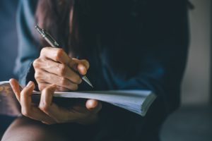 soft focus. Hand high school or university student in casual holding pencil writing on paper answer sheet. Sitting on lecture chair taking final exam or study attending in examination room or classroom