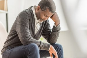 Older man sitting alone at home, elbow on knee with hand to face