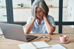 Middle-aged woman sitting at her desk with laptop, glasses, and cup of tea nearby