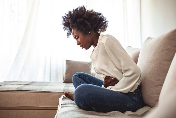 Young woman sitting on couch, holding her stomach in pain