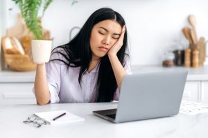 Drowsy woman sitting at desk with a cup of coffee, trying to stay awake