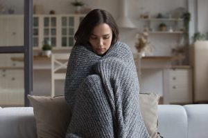 Woman sitting alone on couch, wrapped in gray blanket