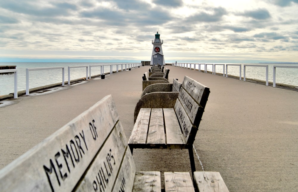 shows memorial benches along the middle of a inlet walkway with lighthouse are end of wharf