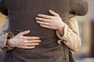 man in brown sport coat hugging woman, focus on man's back and woman's hands as they hug